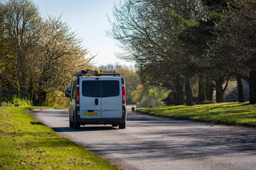 Fototapeta premium Van Driving on Curving Suburban Road Through Green Landscape on Sunny Afternoon in England UK
