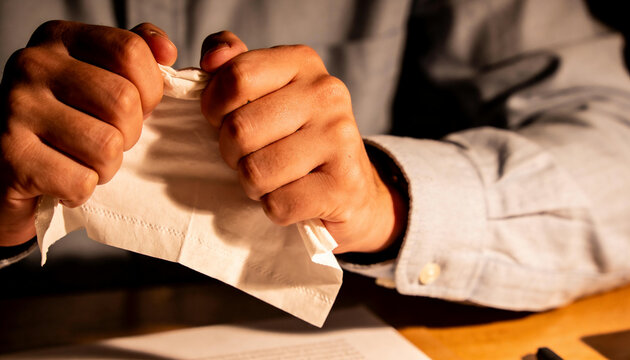 Tearing worker hands gripping tissue on desk in dim office, buttoned cuff, printed-paper and pen