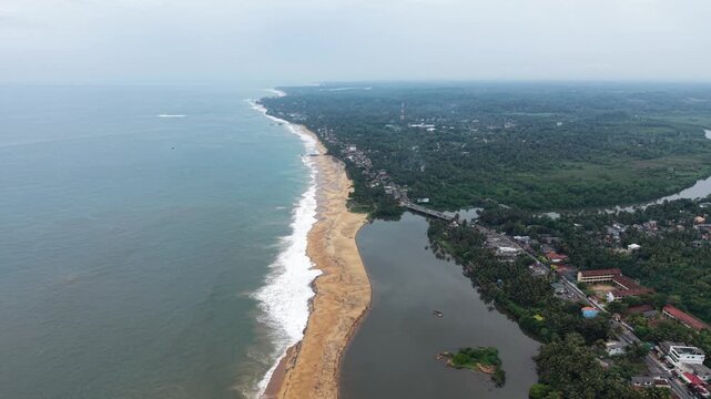 Aerial view of Mahamodara Lake separated from the ocean by a sandy beach strip with lush tropical greenery and coastal buildings in Galle, Southern Province, Sri Lanka.