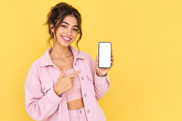 Naklejka premium Young woman in pink outfit pointing at a smartphone with a blank white screen