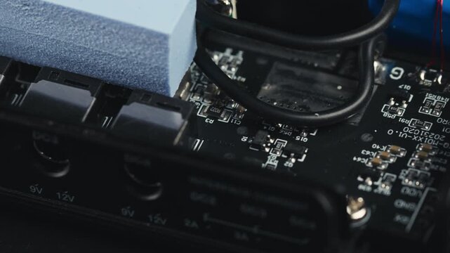 Macro slider shot of a disassembled UPS circuit board. Selective focus moving over blue thermal pad, wires, and various micro electronic components on PCB surface. High-tech engineering background.