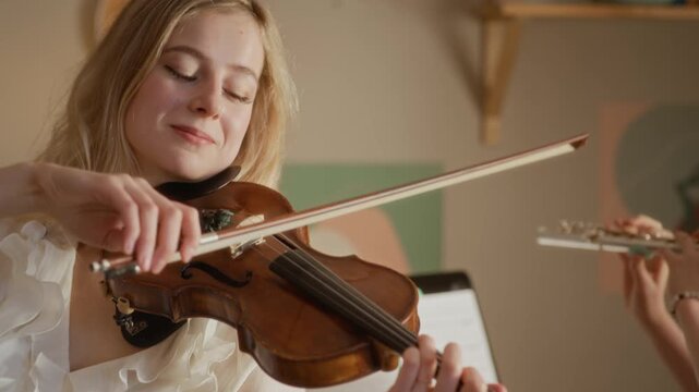 Handheld shot of child playing flute and young adult Caucasian female teacher playing violin during home music lesson. Footage is ideal for promoting private music education and tutoring services