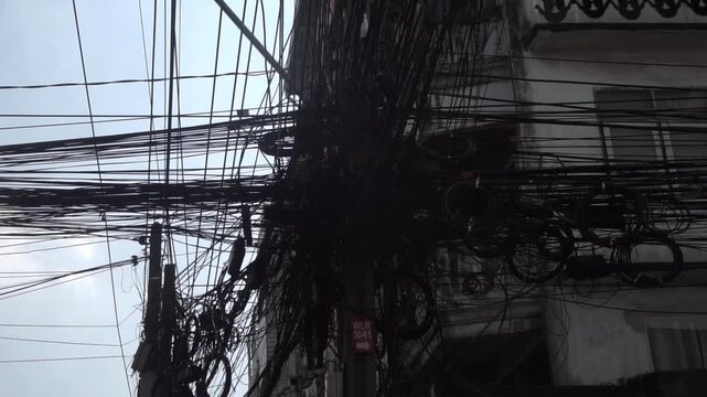 Messy power wires are tangled on the electrical pole, creating a chaotic arrangement of internet cables and powerlines in Thailand.