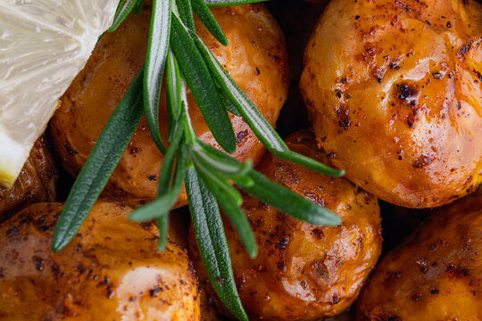 Close up freshly crispy roasted potatoes are placed in a bowl with a slice of lemon and sprigs of rosemary on top. Homemade comfort food and healthy side dishes. top view