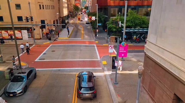 Drone footage captures dynamic city intersection with cars and pedestrians in motion.
