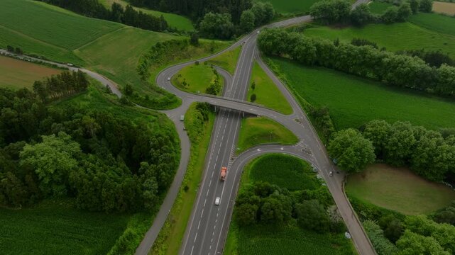Top-down aerial view of a clean, modern road interchange integrated into the verdant, rolling agricultural landscape of S o Miguel Island, surrounded by lush green fields and dense patches of forest