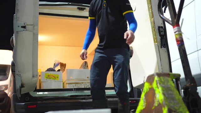 Male worker loading styrofoam boxes of freshly caught fish into a refrigerated delivery vehicle