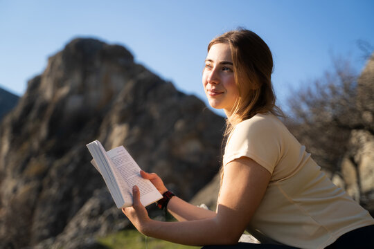 Young female reader enjoying literature outdoors with mountain view.

