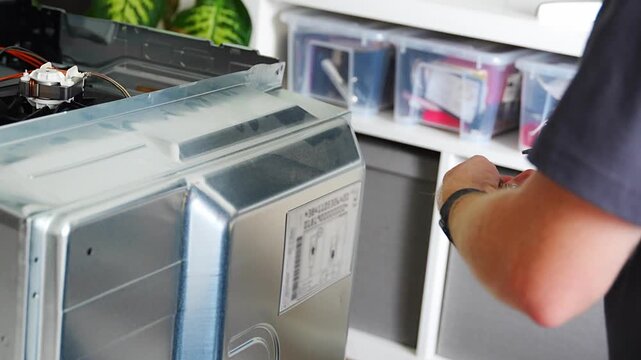 Technician removing rear cover of electric oven before diagnostics and repair. Accessing internal components concept
