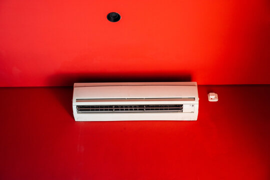 White wall mounted air conditioner on bright red wall with dramatic lighting and minimalist interior concept.