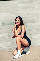 Smiling fit woman in black workout outfit kneeling on outdoor steps showing athletic sneakers and...