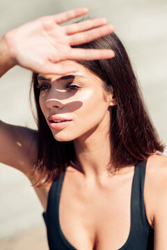 Young woman portrait shielding her eyes from the sun with hand casting a shadow on her face outdoors, summer beauty and natural light close-up
