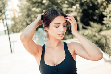 Young fit woman adjusting hair after outdoor workout portrait in sports bra, healthy lifestyle and...