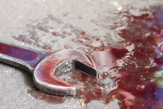 Close-up of a metal spanner wrench lying in a puddle of leaked dark red hydraulic fluid on a concrete floor.