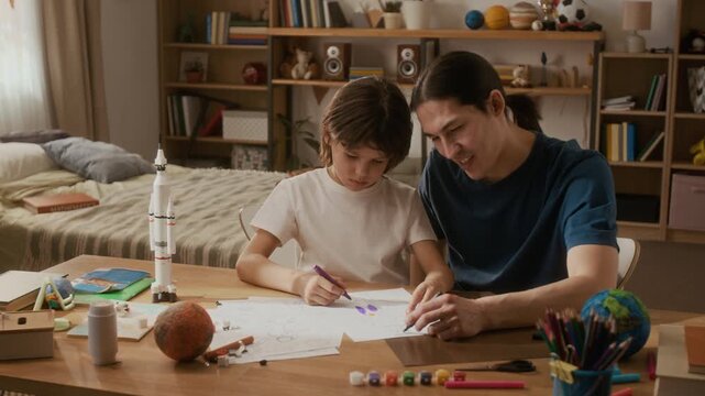Asian father and young multiethnic boy drawing space rocket on paper at desk. Footage is ideal for commercial videos promoting homeschooling and creative childhood development