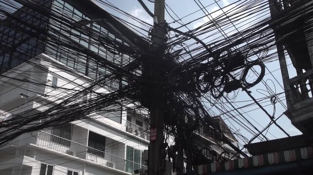 Messy power wires are tangled on the electrical pole, creating a chaotic arrangement of internet cables and powerlines in Thailand.