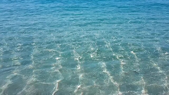 Crystal clear turquoise sea water with sun glint and ripples on the surface