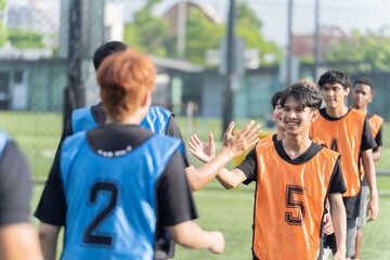 Naklejka premium Southeast Asian soccer players smile and give high fives on an outdoor field before or after a game, showing teamwork, encouragement, and sportsmanship