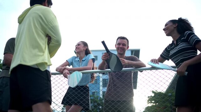 Group of pickleball players gathering court side after a match, sharing conversation and camaraderie in a friendly outdoor sports environment