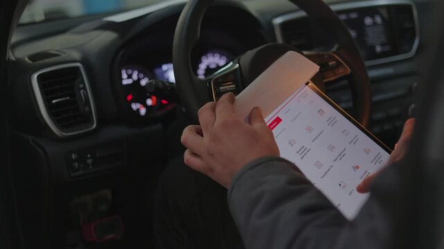 The image shows a close-up shot of a male technician conducting a digital scan of a modern vehicle's systems.The professional worker runs a computer check.A black steering wheel is in front.