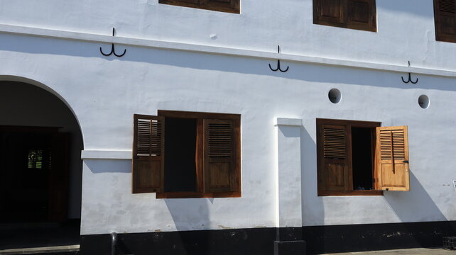 Several wide, brown wooden windows are fitted onto an old white building.