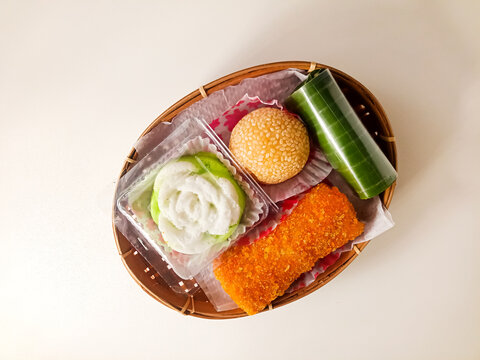 Assortment of traditional Indonesian market snacks (jajanan pasar) including onde-onde, lemper, risoles, and putu ayu served in a woven bamboo basket isolated on a white background.