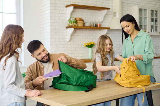 Family parents mother father children packing backpacks. Two schoolgirls prepare at a home kitchen table, organizing supplies for a new school morning. Concept of back to school readiness