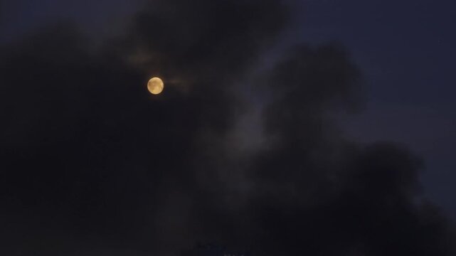 Kyiv, Ukraine - June 2, 2026: Full moon partially obscured by thick black smoke from a fire caused by Russian missile and drone strikes at night.