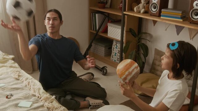 Asian man and multiethnic kid sitting on floor, studying astronomy with planet model and playing with soccer ball. Clip is perfect for e-learning platforms and homeschooling advertisements