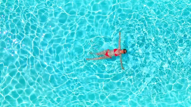 Top down view of a woman in pink swimsuit swimming on her back in the pool.