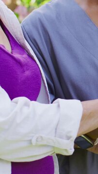 Vertical video: Cradling hand as patient offering it, nurse in grey scrubs checking watch in yard