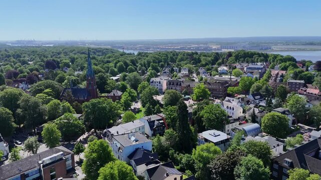 Aerial view of Marktkirche Blankenese surrounded by lush green trees and residential houses with the Elbe river in the background in Hamburg, Hamburg, Germany.