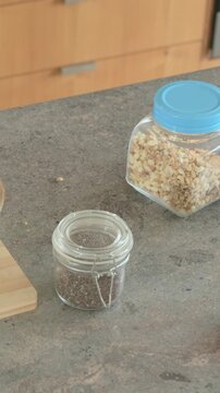 Vertical video: Reaching female hand spooning cream onto bananas on counter for breakfast with chia