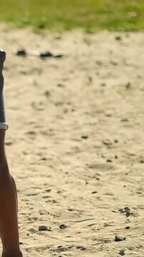 Vertical video: Foot nudging white ball on sand, boy in rolled shorts walking to grass, copy space