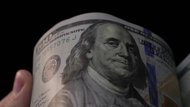 Close-up of hand flipping through stack of U.S. hundred dollar bills in slow-motion