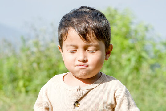 Portrait of a young boy with eyes closed, expressing a pouting or thoughtful emotion outdoors in nature