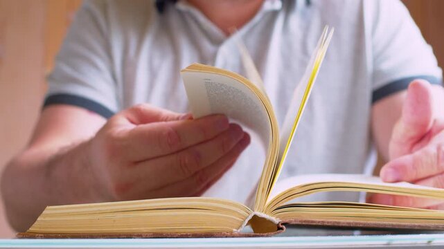 Cinematic macro shot of turning old book pages. Defocused man silhouette. Soft warm sunshine.