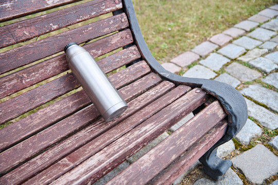 Silver thermos bottle resting on weathered wooden park bench with stone path and grass