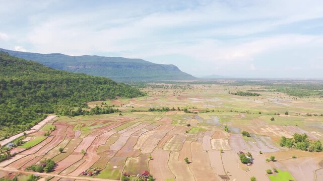 Cinematic drone footage of the tropical forest and agricultural landscape near Khamtay, Attapeu Province, Laos. The aerial view captures the transition from dense jungle on the hillside to the cultiva