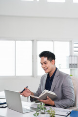 Obraz premium Businessman hand holding pen writing on notebook, work on laptop computer in modern office.