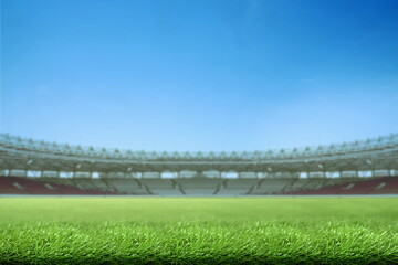 Naklejka premium Low-angle view of a vibrant green grass field inside a large, empty sports stadium under a clear blue sky