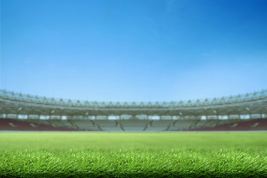 Low-angle view of a vibrant green grass field inside a large, empty sports stadium under a clear blue sky