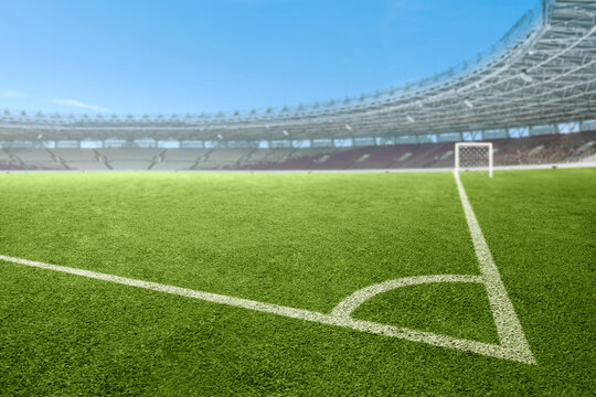 Close-up of a corner kickoff area on a bright green grass soccer field inside a large modern sports stadium under a clear blue sky