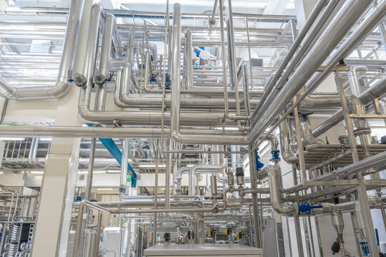 Modern industrial factory interior with stainless steel pipes and processing machinery. Clean automated production line in food, dairy, or chemical plant engineering industry.