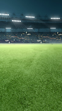 Vertical view of a lush green soccer field in a stadium at night, illuminated by bright floodlights with blurred stands