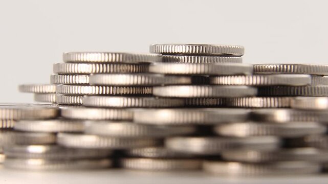 Silver coins stacked in large pile filmed with shallow depth of field, foreground coins blurred, camera pans left to right revealing sharp central stack structure in smooth seamless loop.