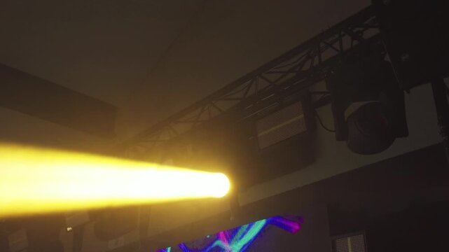 Yellow stage spotlight cutting through smoky concert interior. Close-up of a stage lighting rig mounted on a truss and illuminated with bright yellow light