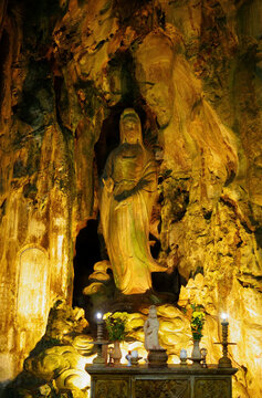 Lady Buddha statue carved inside the Marble Mountains cave in Da Nang, Vietnam. Golden light illuminating Buddhist altar in Huyen Khong Cave.