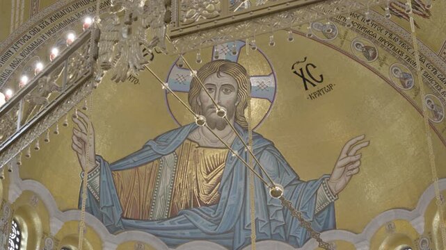 Jesus Christ Pantocrator golden mosaic through the ornate chandelier inside the Church of Saint Sava. Beautiful cinematic real-time video of Orthodox cathedral art. Belgrade, Serbia 22.05.2026