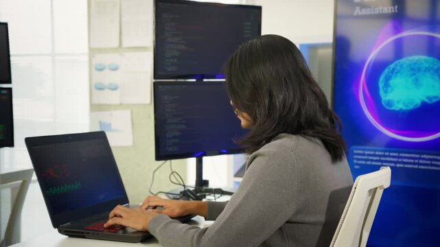 Focused Asian man typing on laptop while using artificial intelligence assistant tool in modern workspace. Generative AI technology, productivity tools, individual freelance work, Tech professionals.